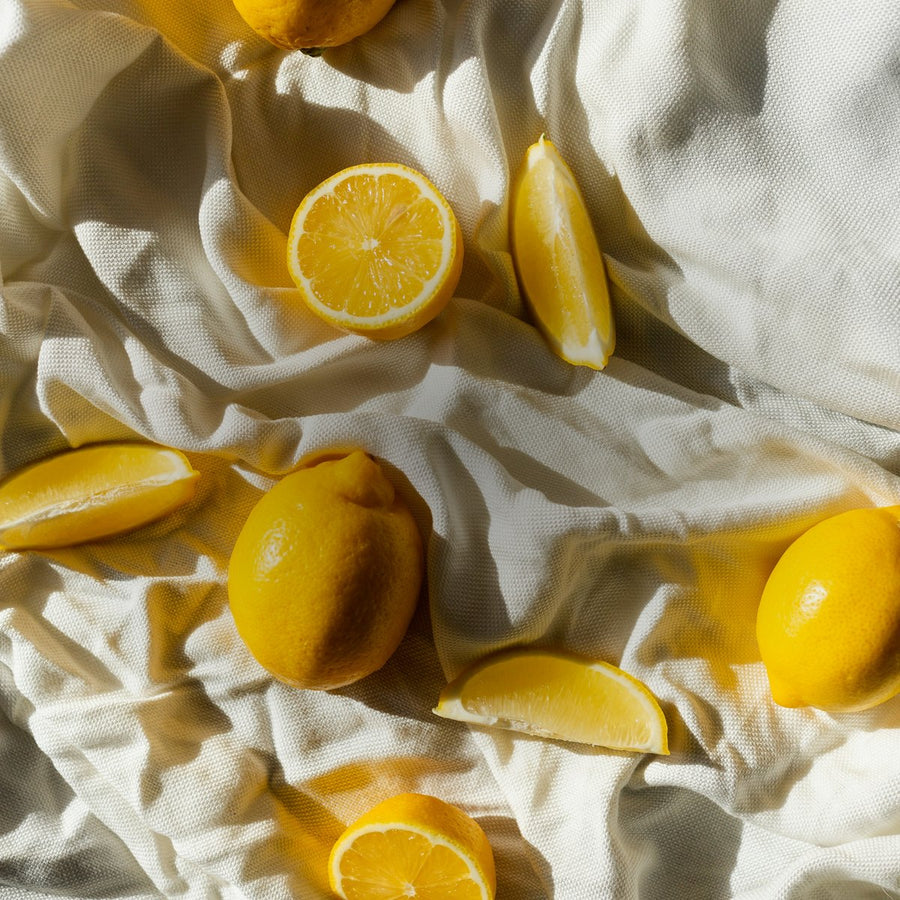Whole and sliced lemons on draped white linen in warm sunlight, citrus fragrance family